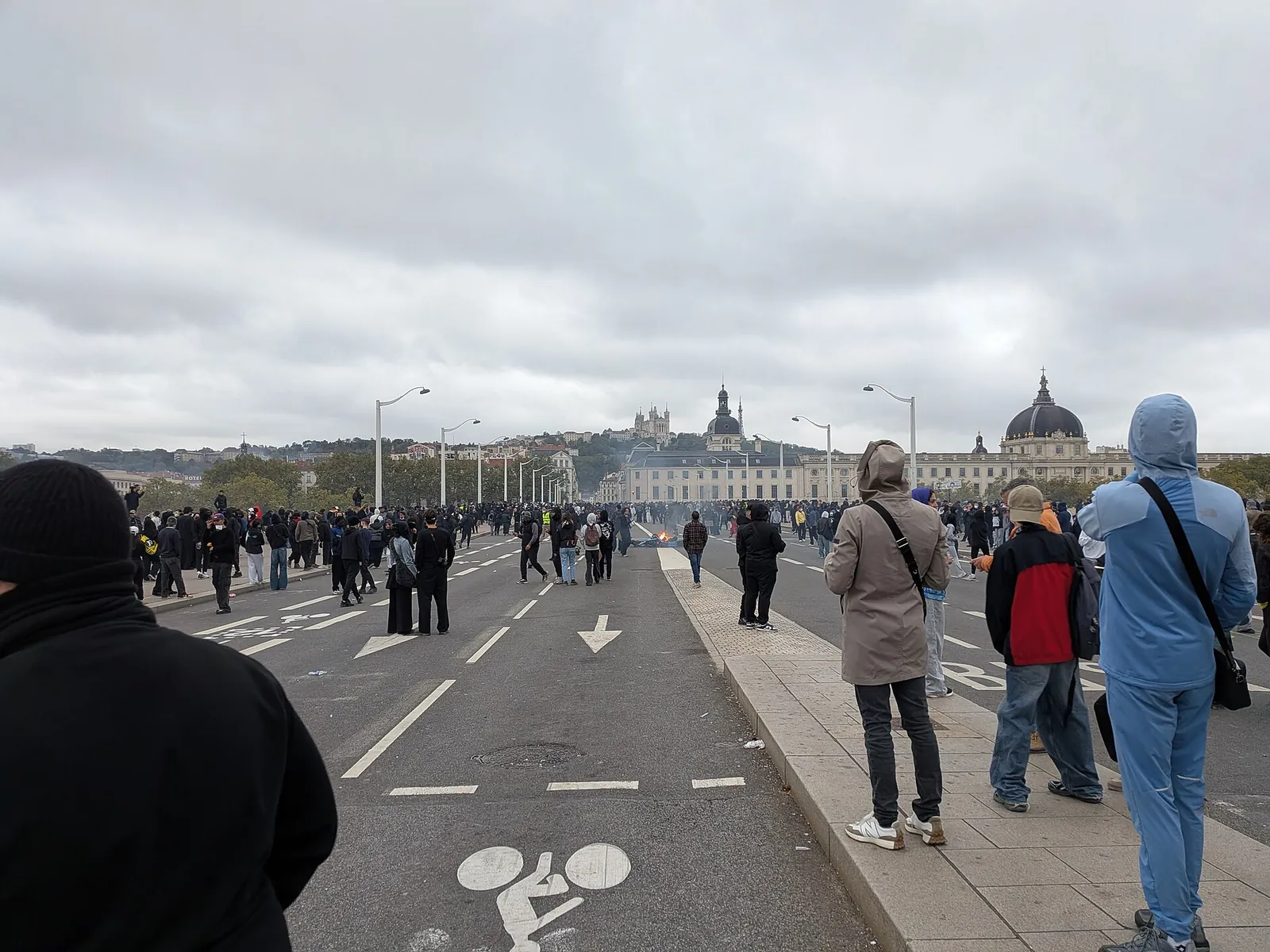 Manifestants et passants sur le pont de la Guillotière à Lyon, sous un ciel gris, pendant la mobilisation du 17 octobre 2026