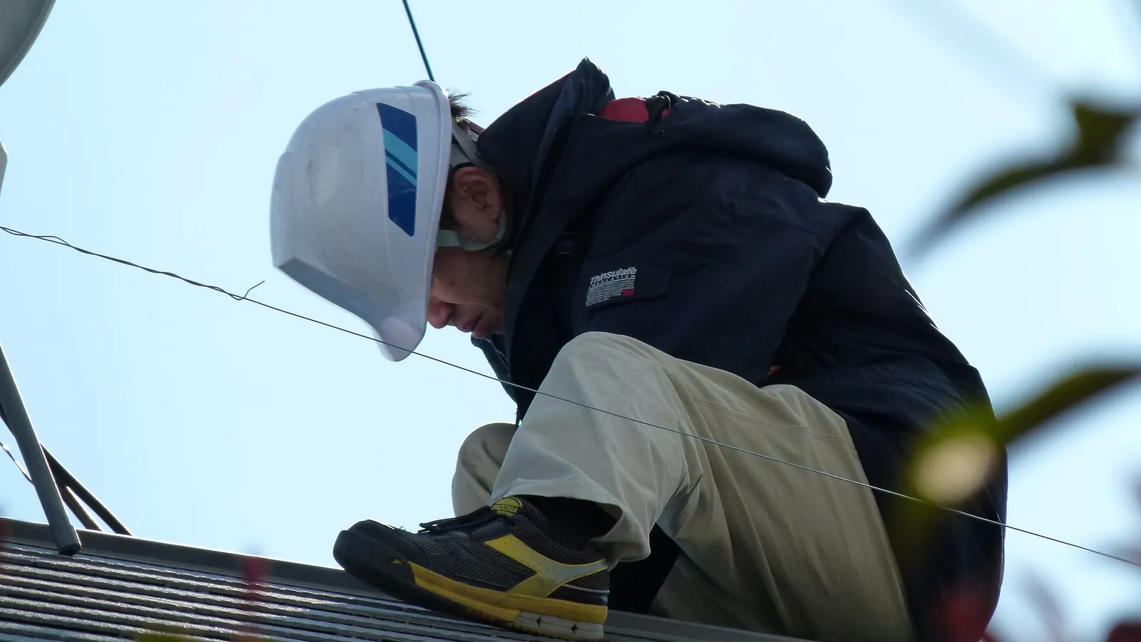 Technicien portant un casque de chantier, accroupi sur un toit pendant l'installation de panneaux solaires